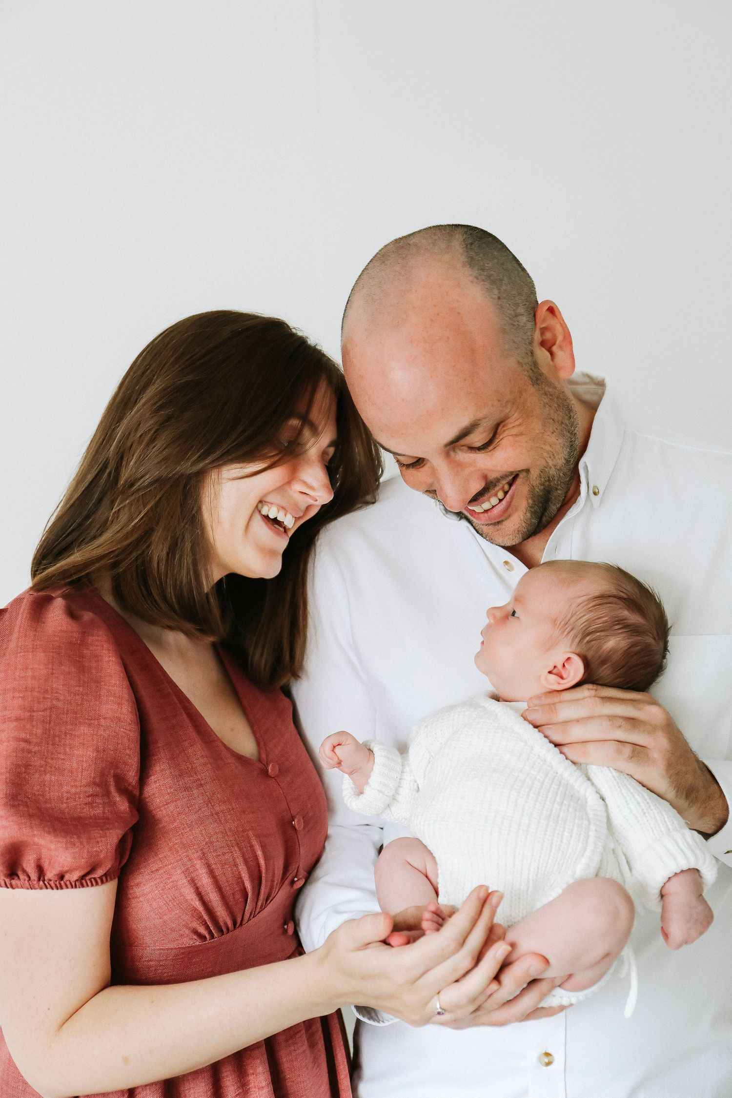 A sweet candid photo showing loving parents with newborn against a white studio backdrop, during newborn photoshoot in Nottingham