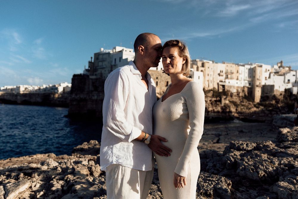 A couple dressed in white share a romantic moment on rocky cliffs overlooking the Mediterranean Sea in Polignano a Mare, Italy.