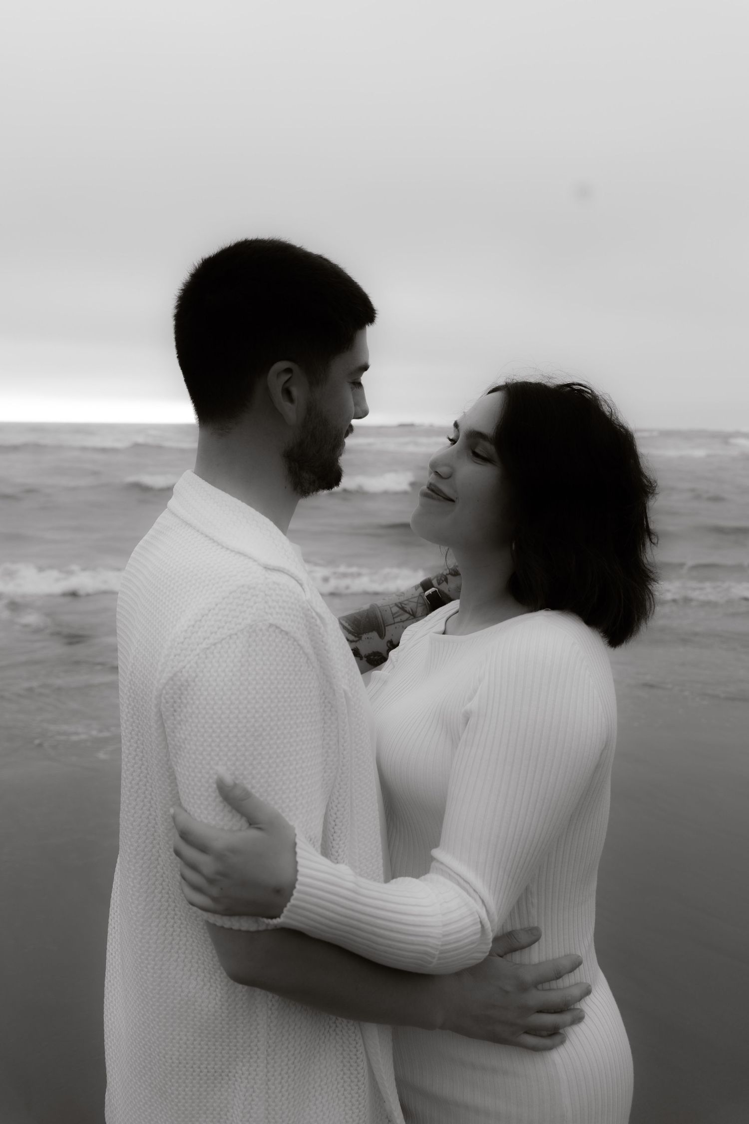 Black and white photo of a couple holding each other close on a beach.