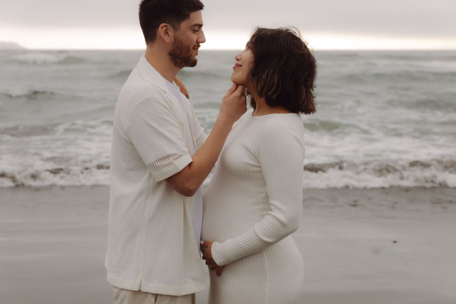 Couple sharing a tender moment on the beach, man gently touching womans face.