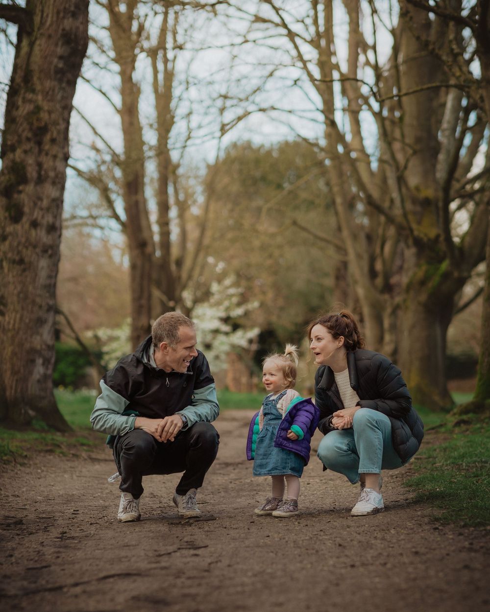 People crouching down together on a dirt path surrounded by trees.
