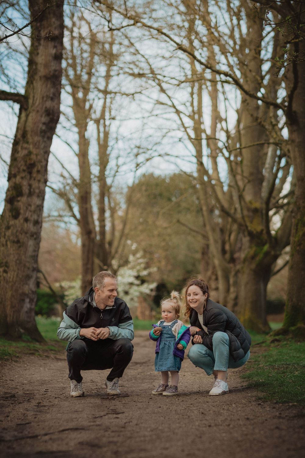 People crouching down on a dirt path surrounded by tall trees in a park.