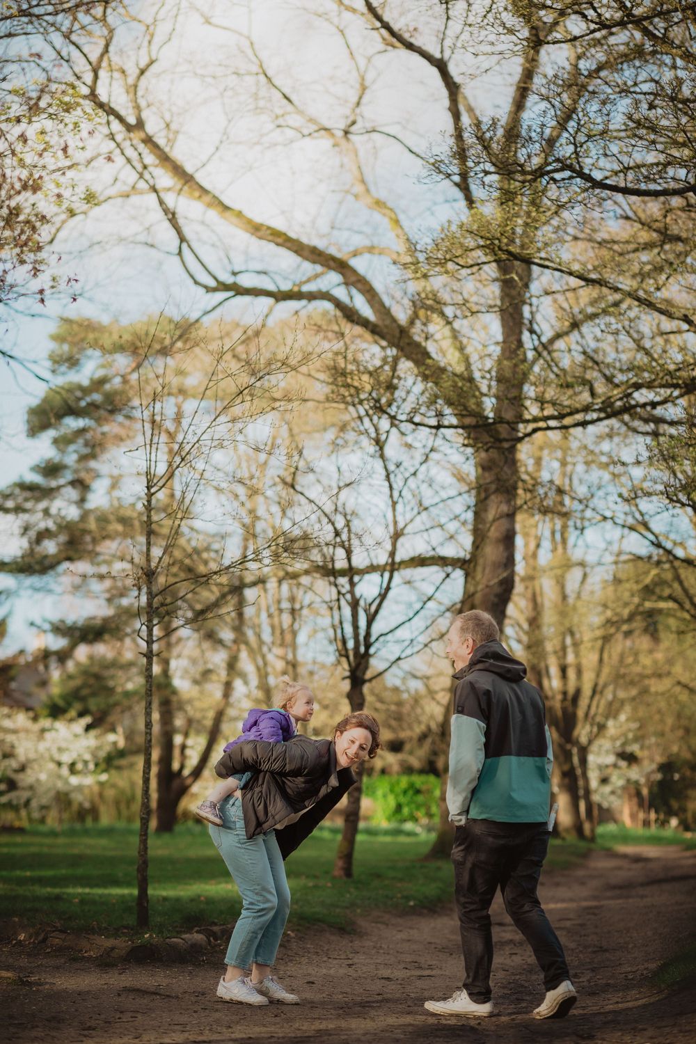 Three people walking along a woodland trail surrounded by bare trees in early spring.
