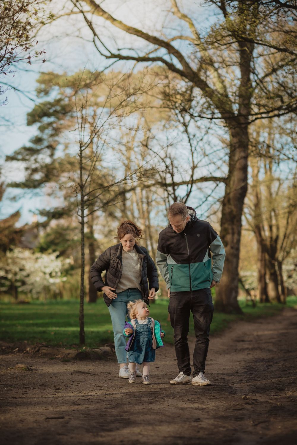 Family takes a stroll together along a wooded path on a sunny afternoon.