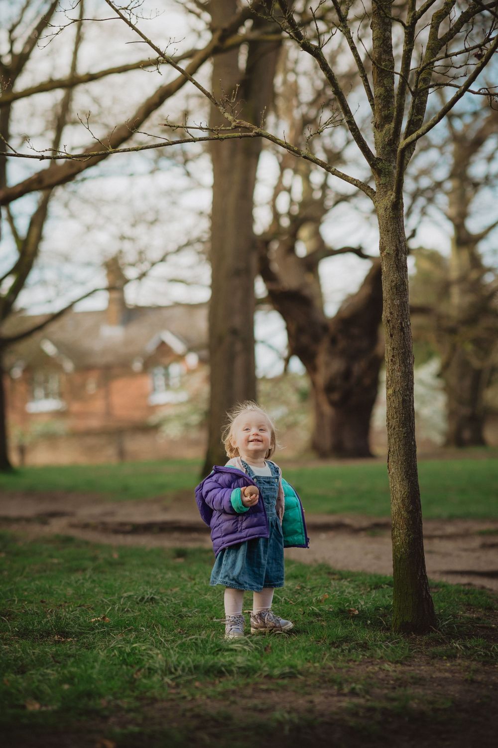 A small child playing joyfully among trees in a park setting.
