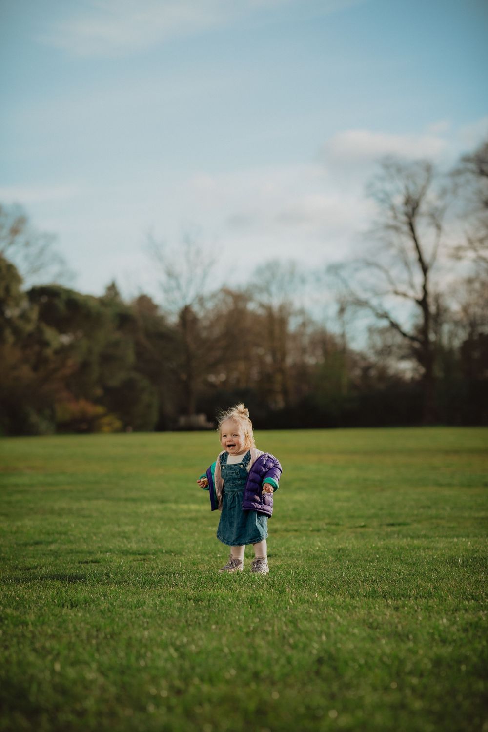 A small child wearing denim overalls runs across a grassy field on a spring afternoon.