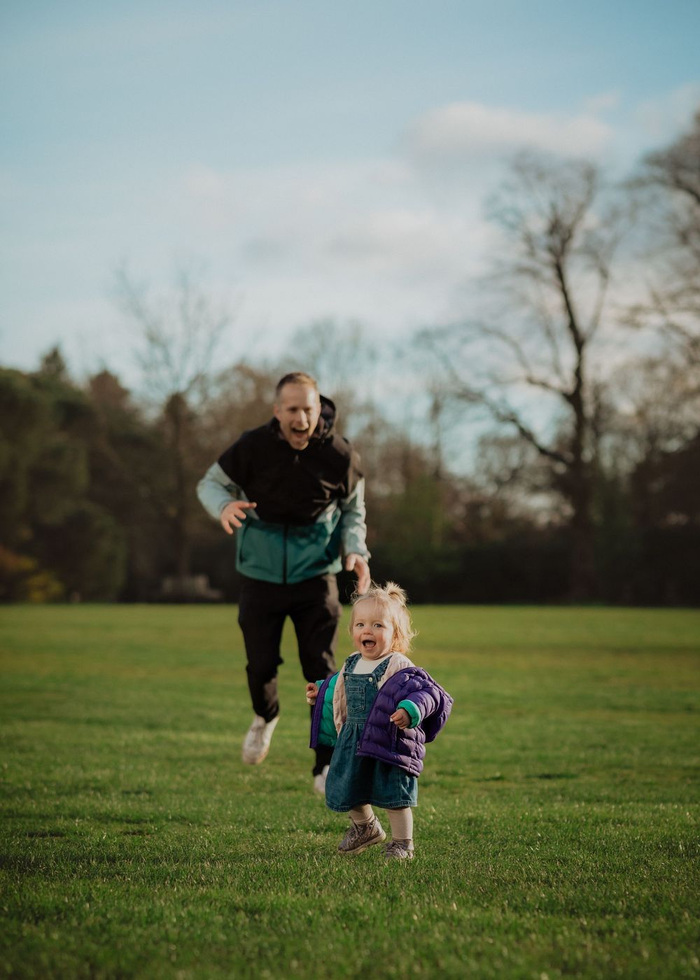 People running and playing together on a lush green field in a park setting.