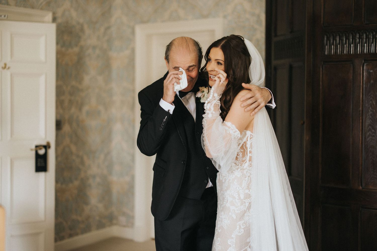 An emotional first look moment at a wedding ceremony showing a bride in white lace and her father in a black suit.