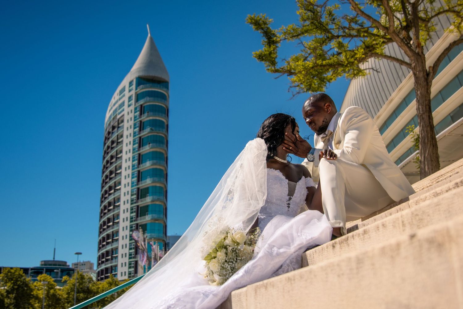 Wedding couple sitting on urban steps with modern glass building in background.