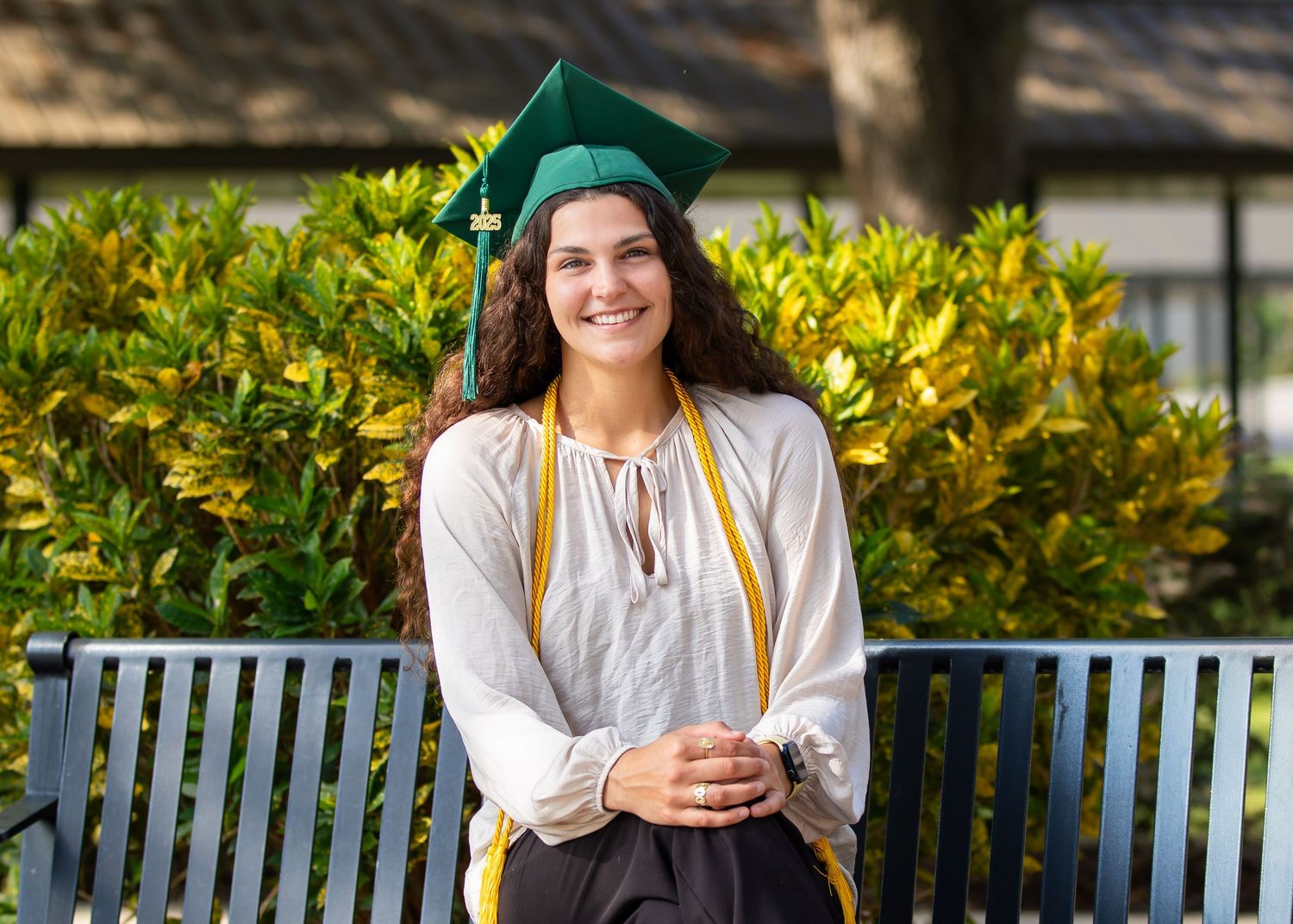 Outdoor graduation portraits with greenery and yellow flowers in background.
