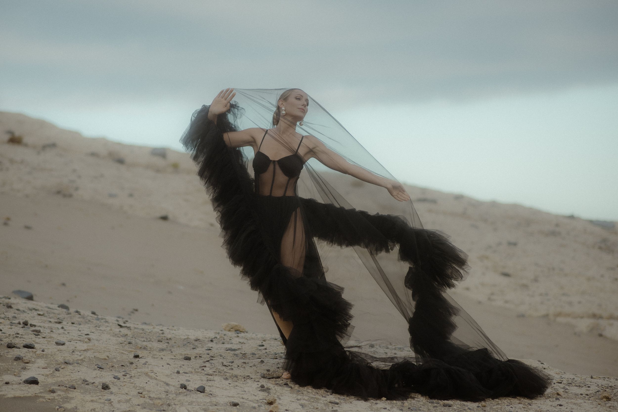 Dramatic desert fashion photo with flowing black fabric and sheer veil against sandy dunes in ethereal lighting in the south of Tenerife.