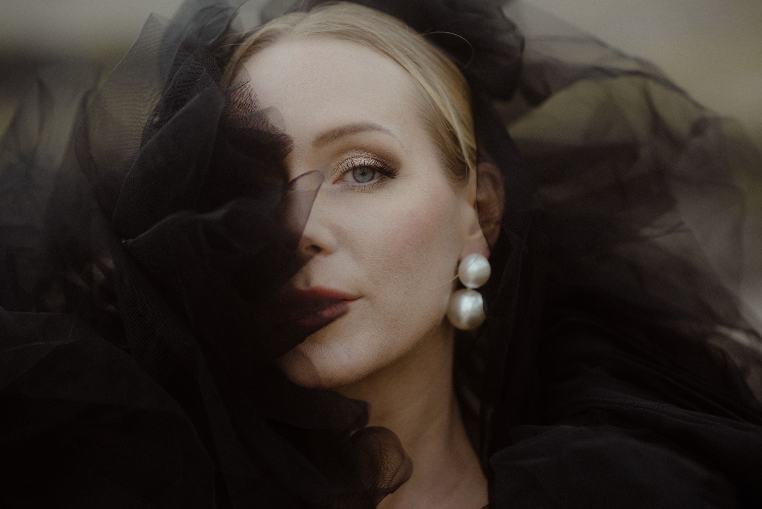 Artistic portrait featuring dramatic dark veil movement and pearl drop earrings against a moody background in the south of Tenerife.