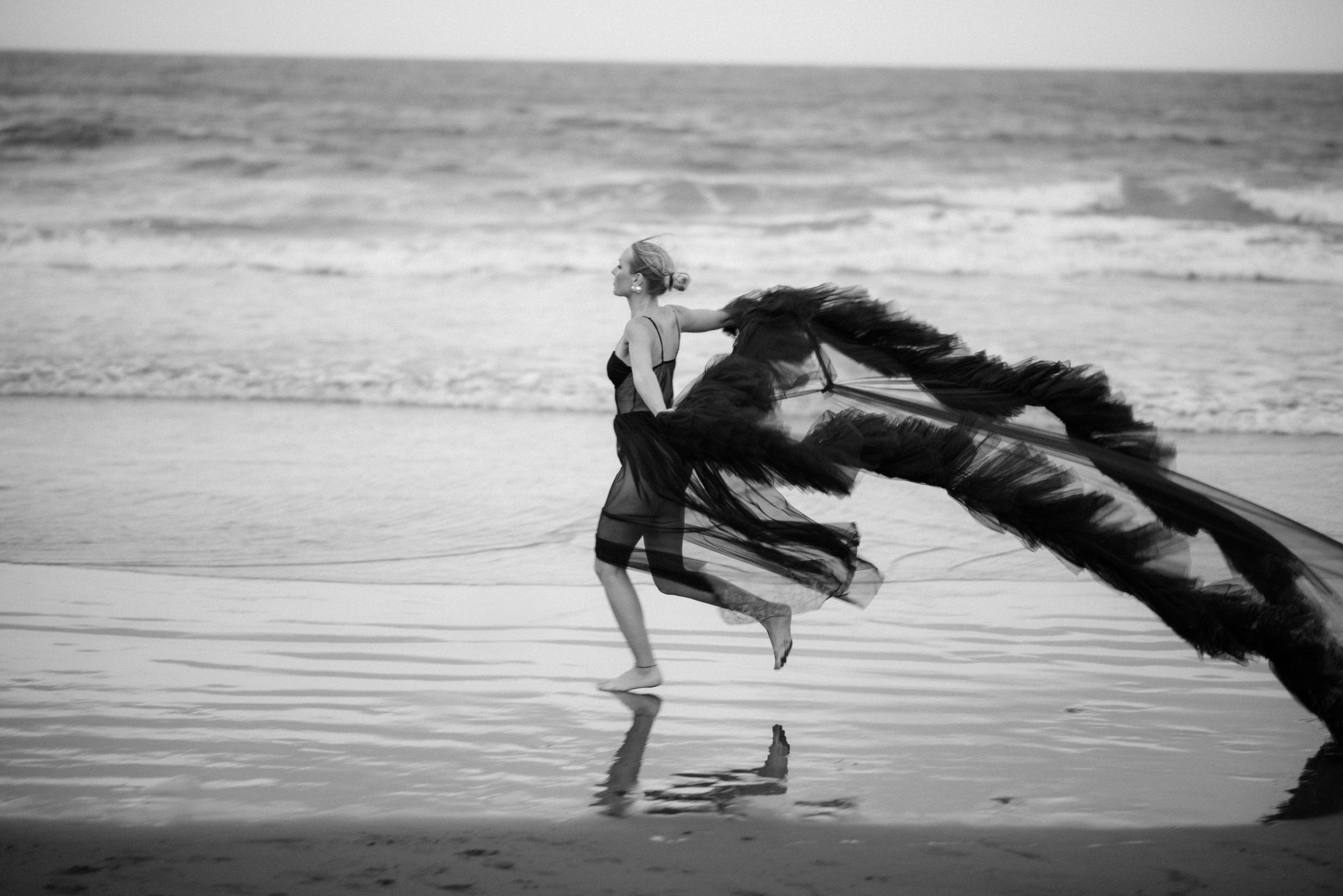 Figure dances on a beach with flowing black fabric billowing in the wind against an ocean backdrop in the south of Tenerife.