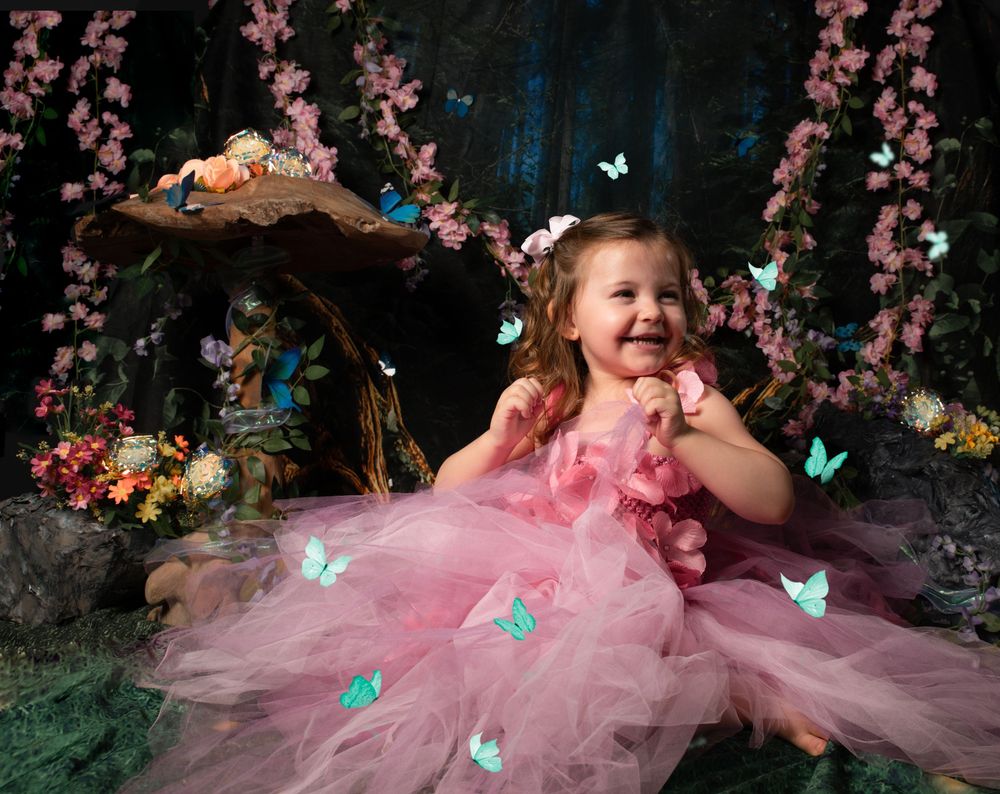 A magical woodland scene with pink cherry blossoms and glowing butterflies surrounding a young child in a flowing pink tulle dress.
