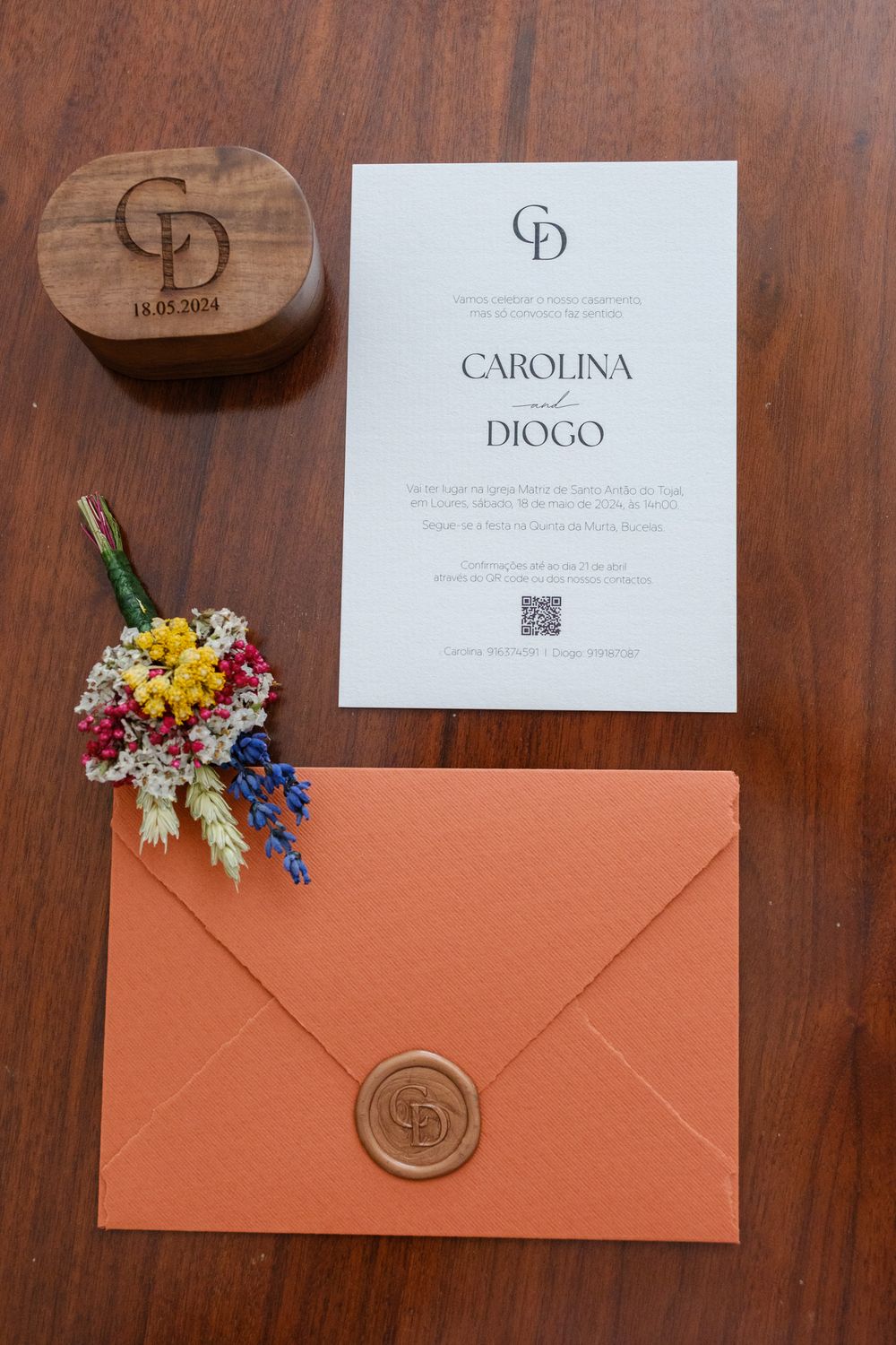 Wedding invitation suite with coral envelopes, wax seals, and colorful floral accents on wooden surface.