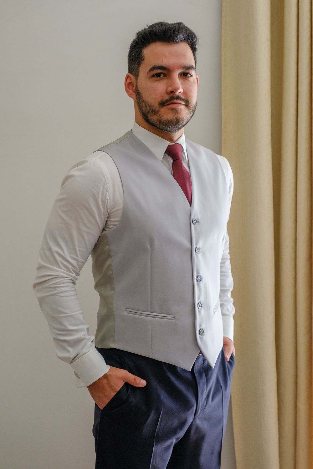 A person in formal attire wearing a light grey vest and red tie poses confidently.