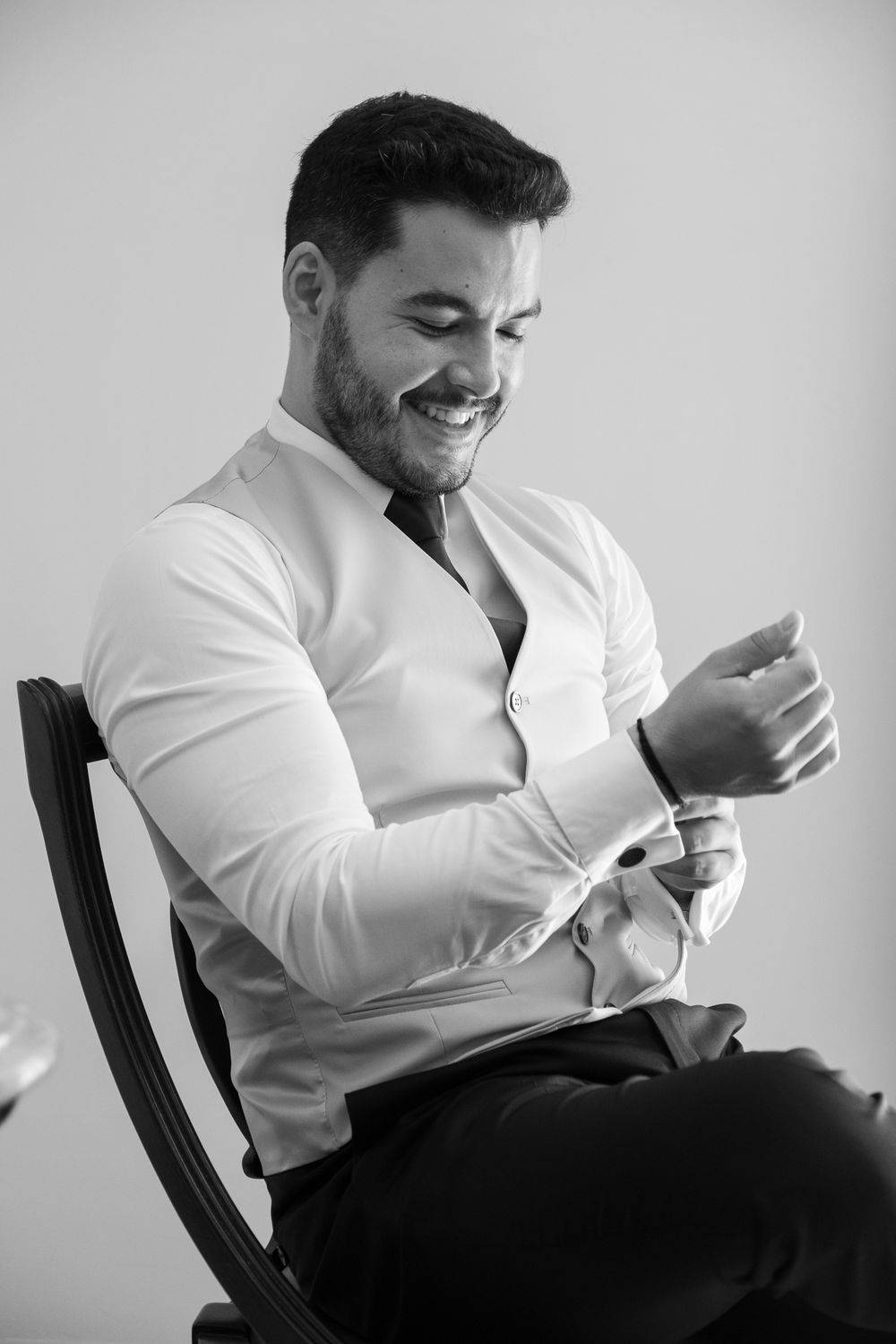 A black and white portrait of someone laughing while adjusting their shirt cuffs.