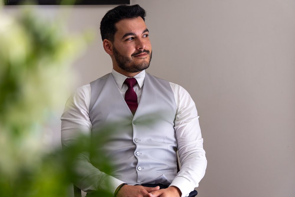 A person in business attire with a red tie smiles warmly while seated.