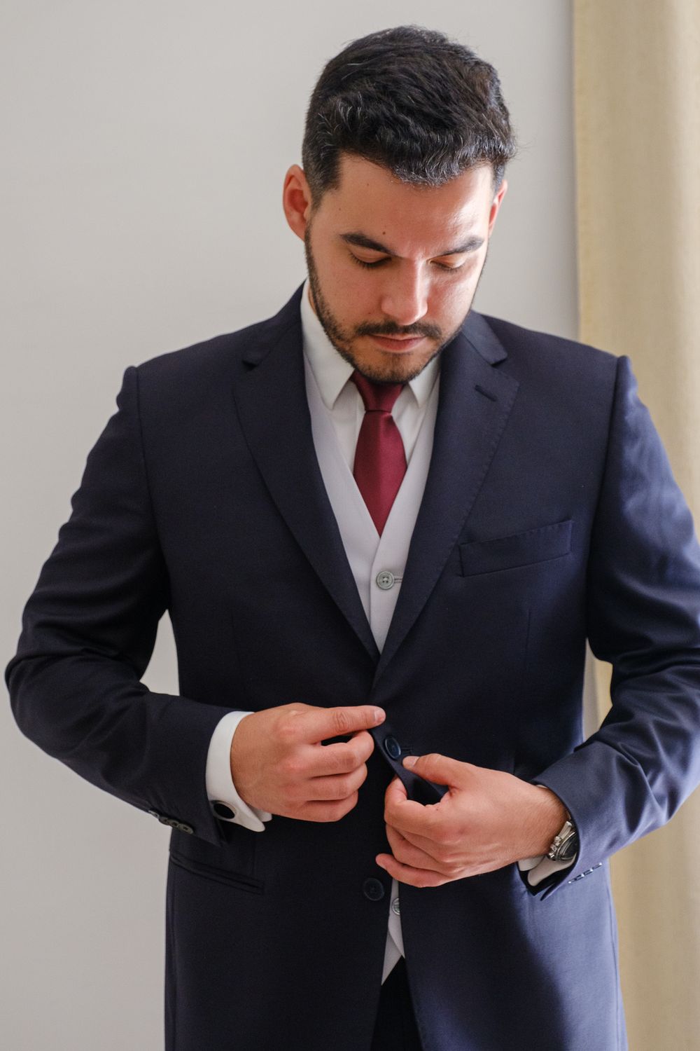 A person in a navy suit and red tie adjusts their jacket buttons.