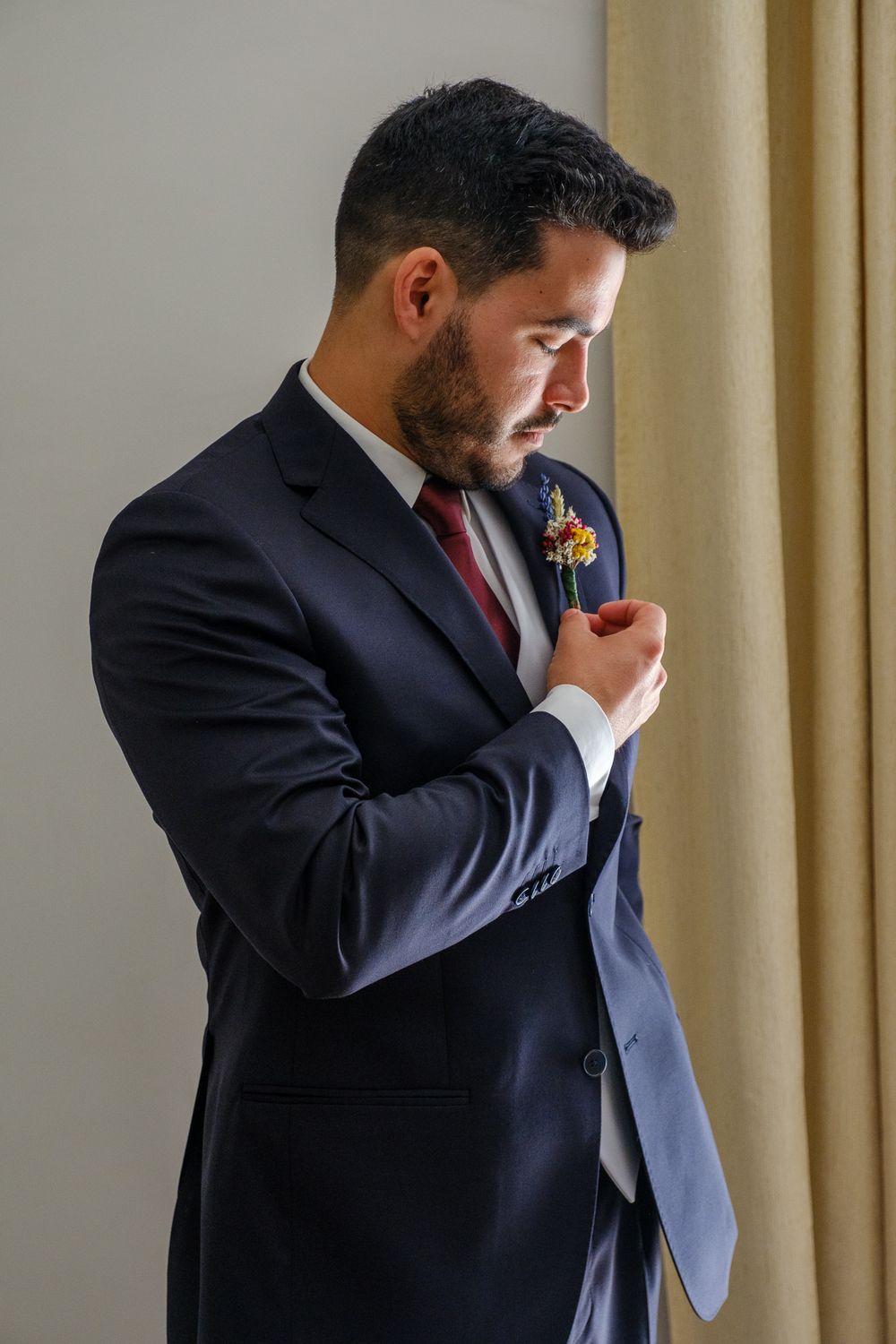 A person in formal attire adjusts their boutonniere while wearing a dark suit.