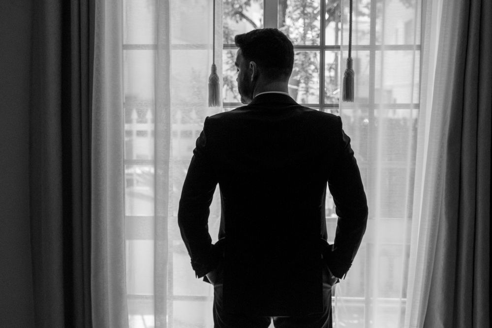 A silhouette of a person in a suit standing by a window with hands in pockets.