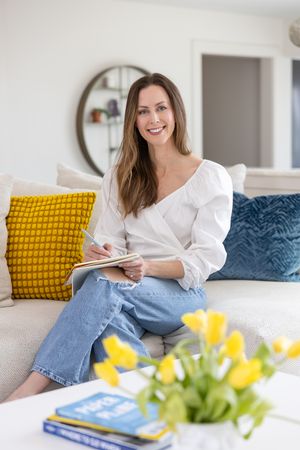 Jessica Stegner Seattle SEO consultant woman business owner branding sitting in living room writing in notebook smiling with tulips and book