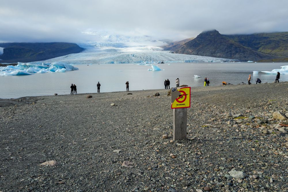 Visitors stand on a rocky overlook viewing a glacial lagoon filled with blue icebergs in Iceland.