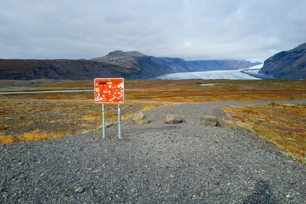 Warning sign stands in foreground with glacier and mountains visible in distance.