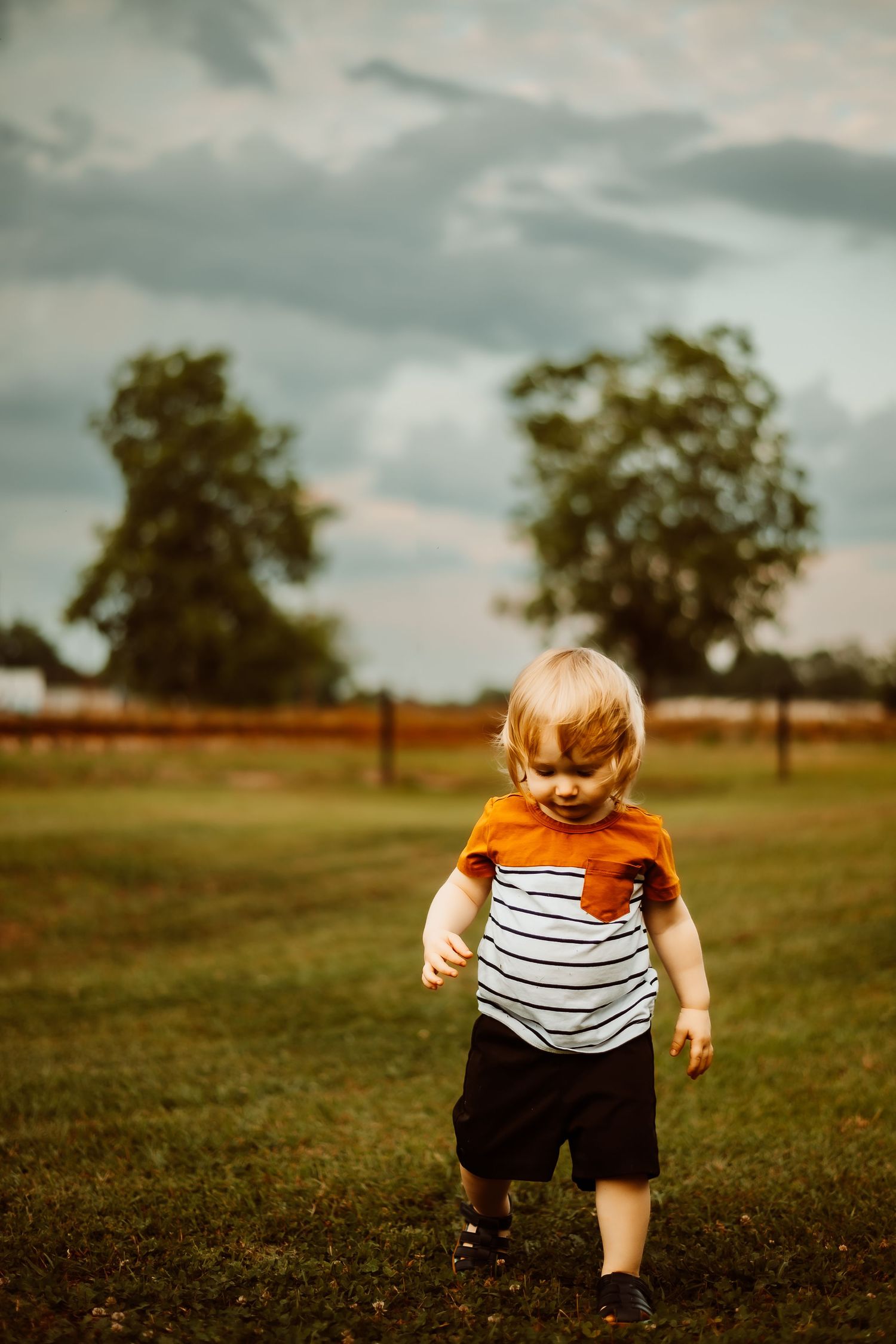 Child in orange striped shirt running across grassy field.