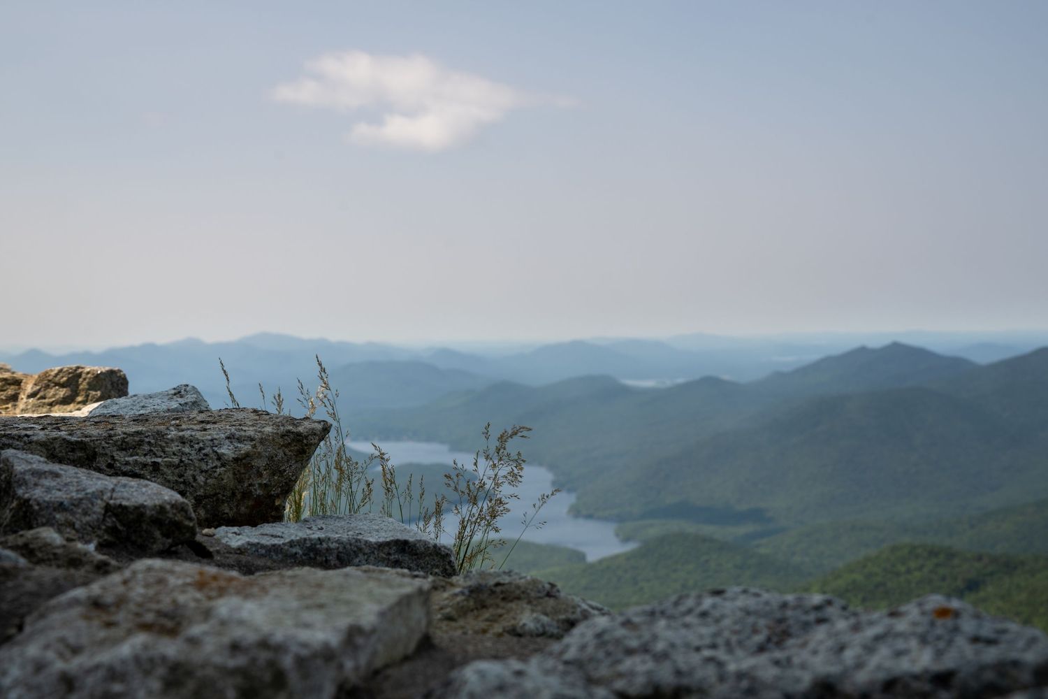A panoramic mountain landscape with rolling hills and blue ridges stretches into the misty distance under a cloudy sky.