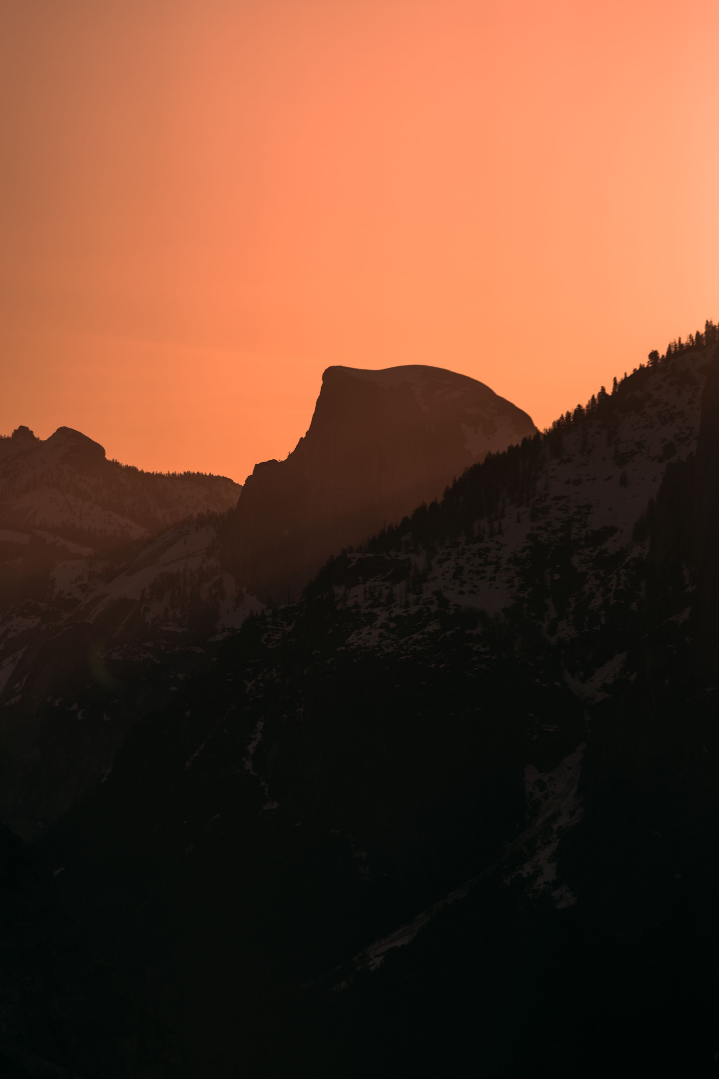 Silhouetted mountain range against an orange sunset sky creating a dramatic alpine panorama.