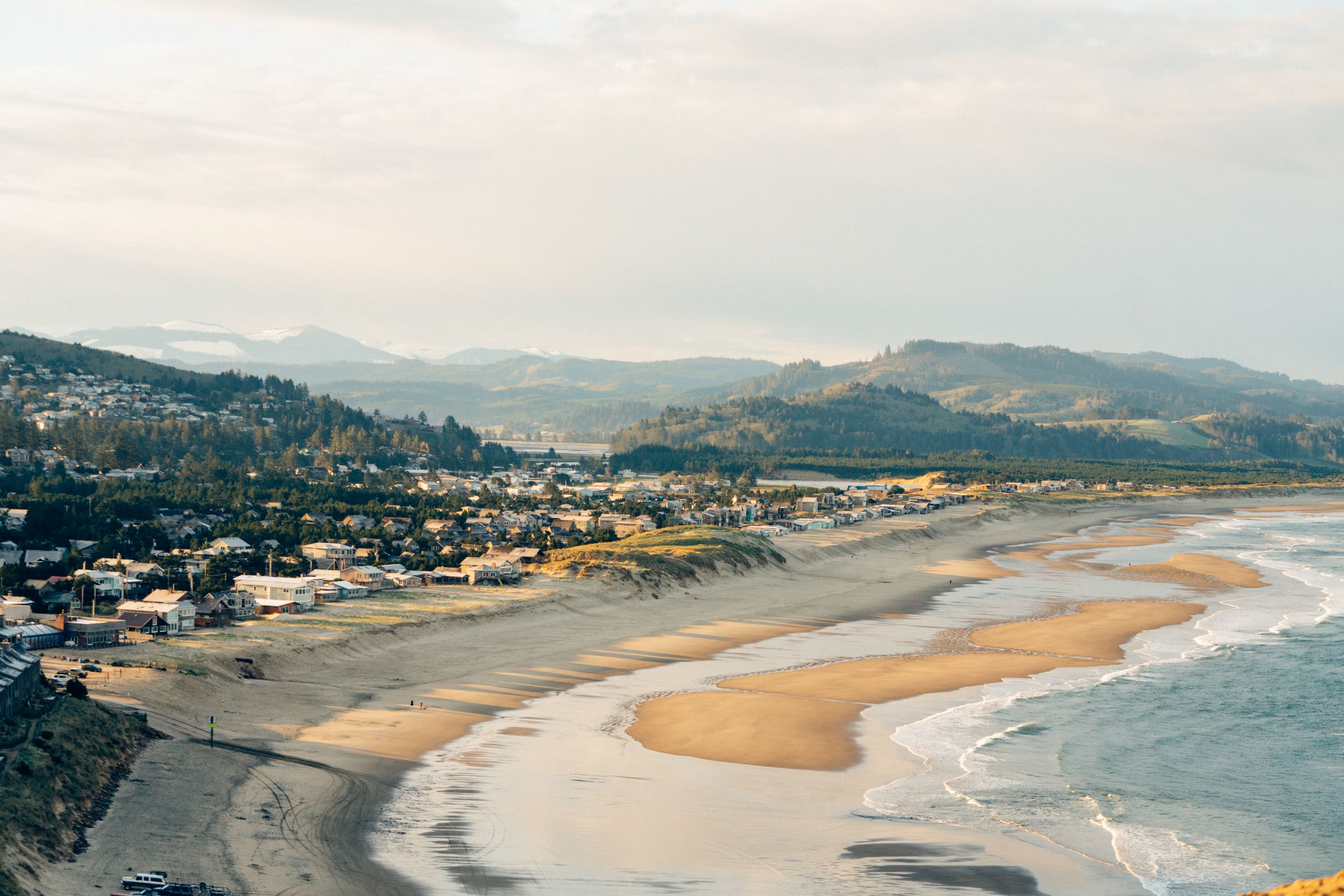 Panoramic view of a curved coastline with sandy beach and mountains in the distance.