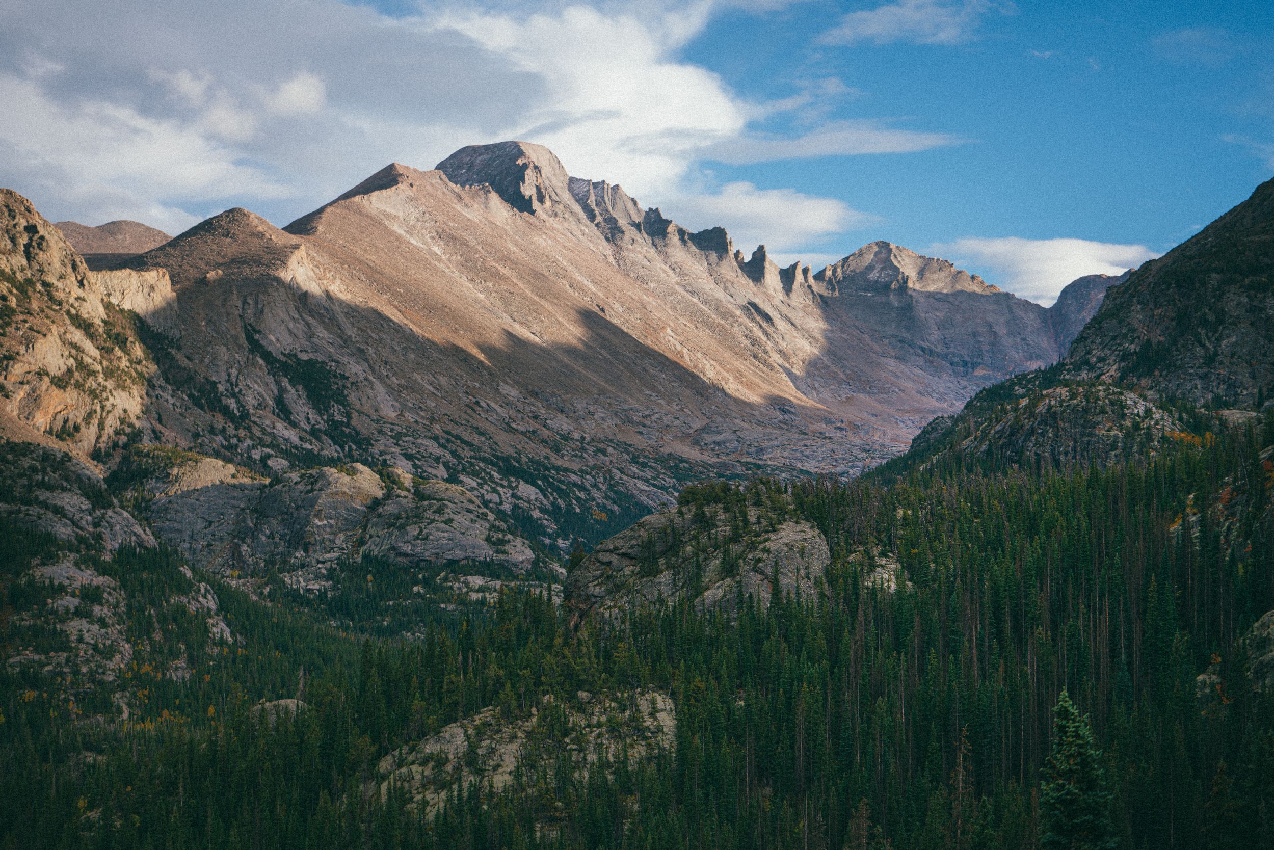 Majestic mountain peaks rise against blue sky in rugged wilderness landscape.