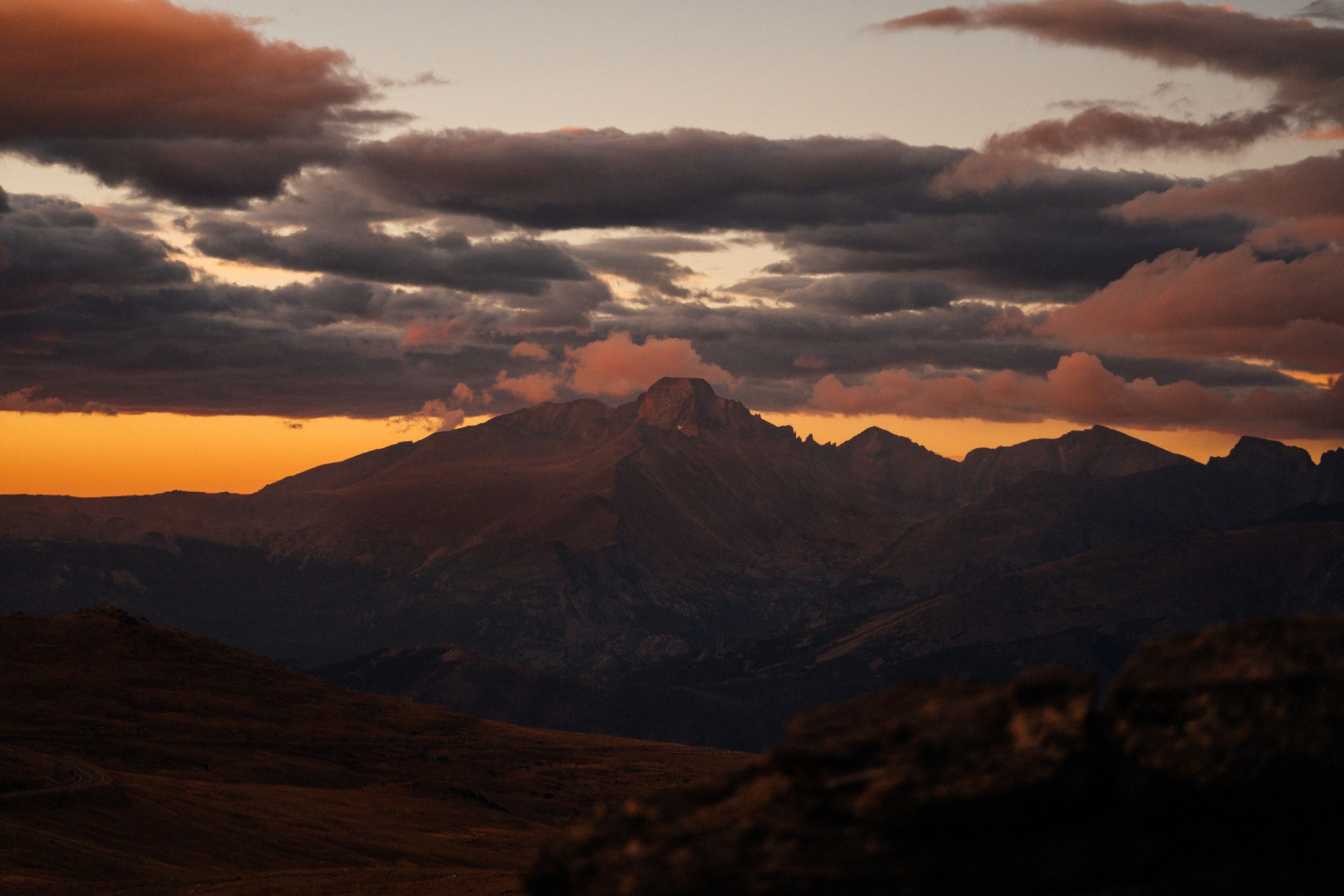 Dramatic sunset illuminates rugged mountain peaks with golden light against a dark cloudy sky.