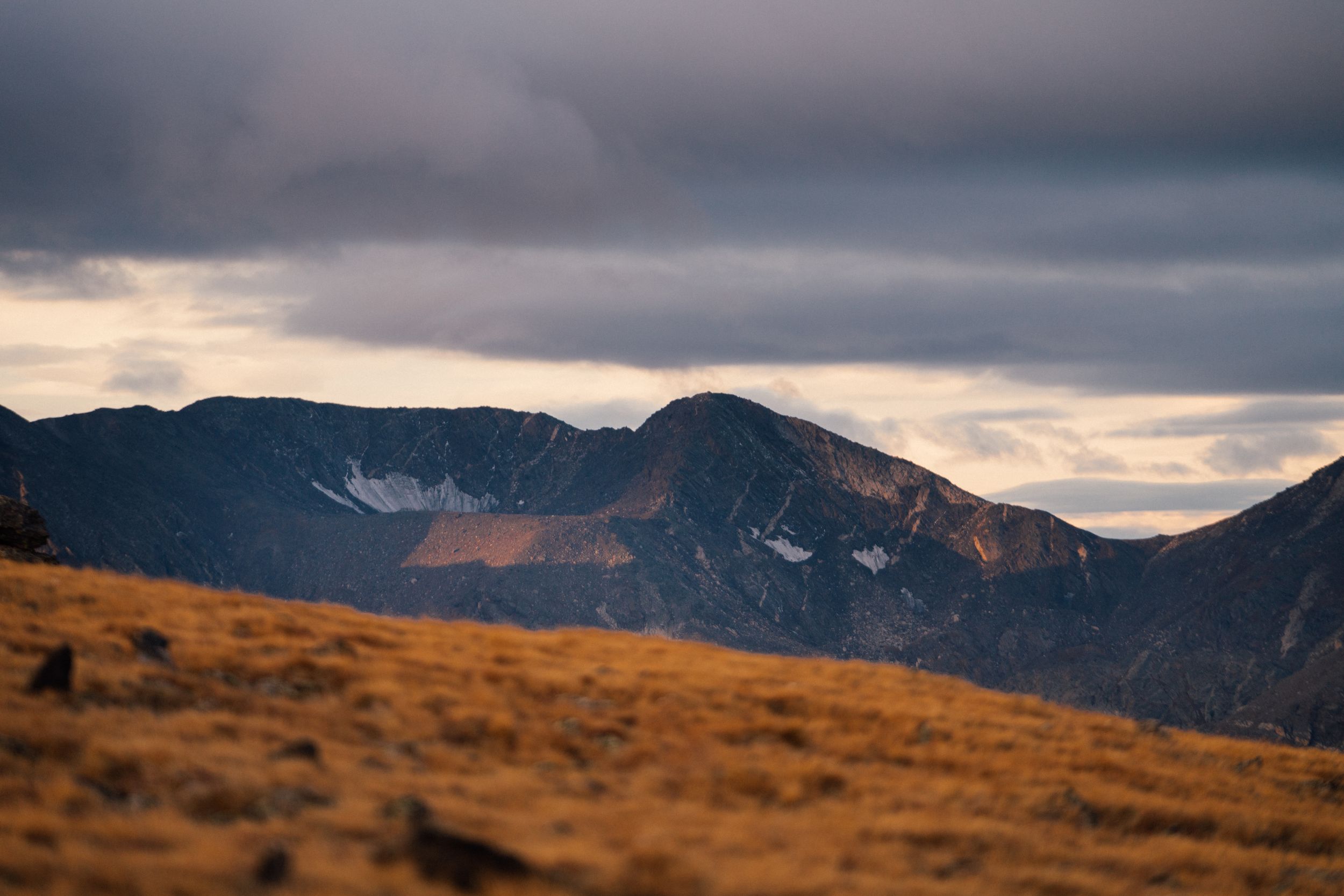 Snow-capped mountain peaks under moody overcast skies during golden hour.