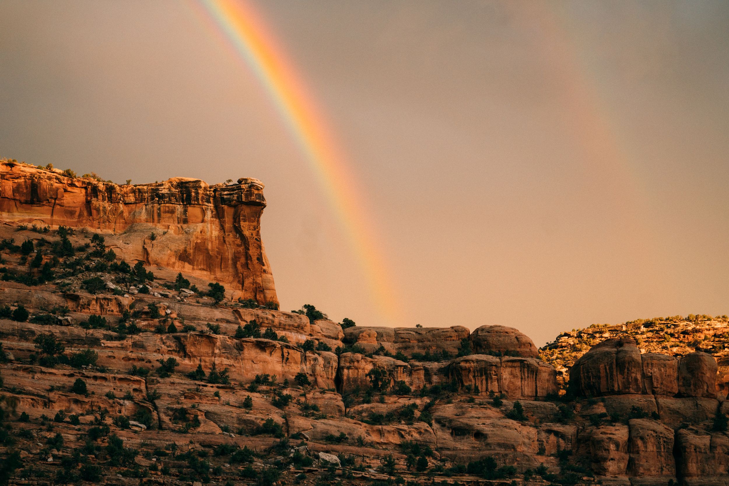 Vibrant rainbow arches over desert rock formations during sunset.