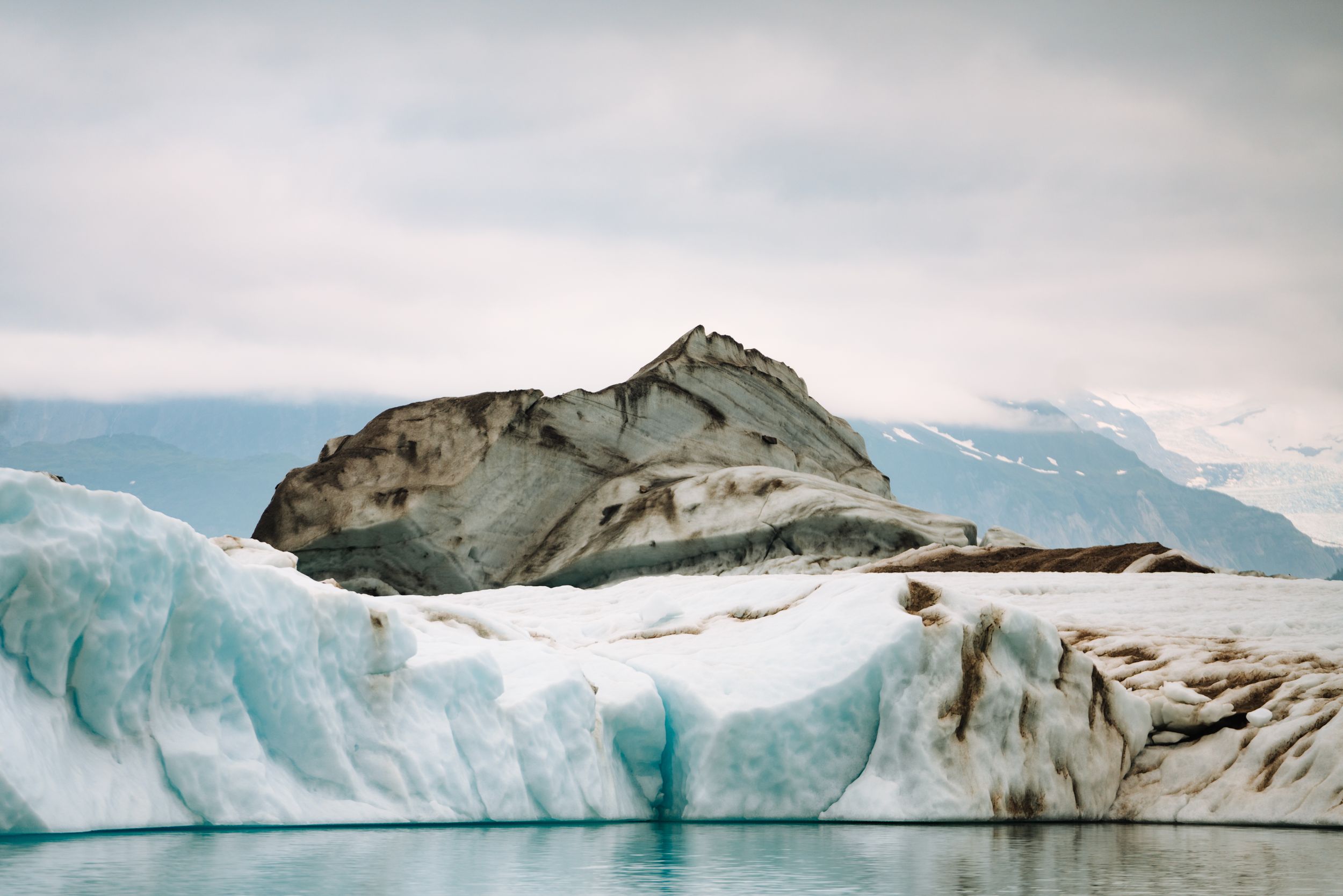 Massive blue glaciers and ice formations stretch across a rugged mountain landscape in Alaska.