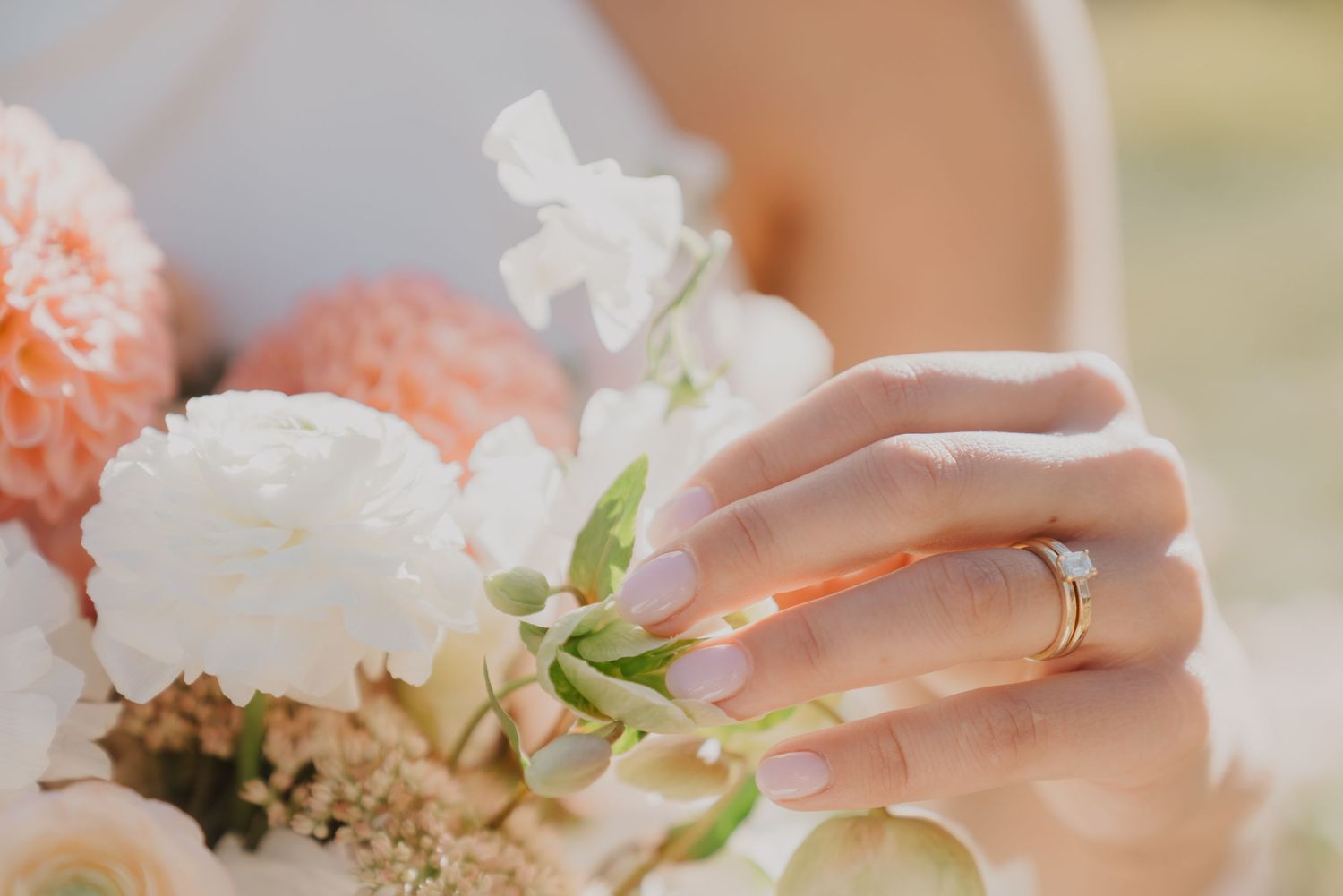 Close-up of bride's hand with wedding ring holding delicate white and peach flowers.