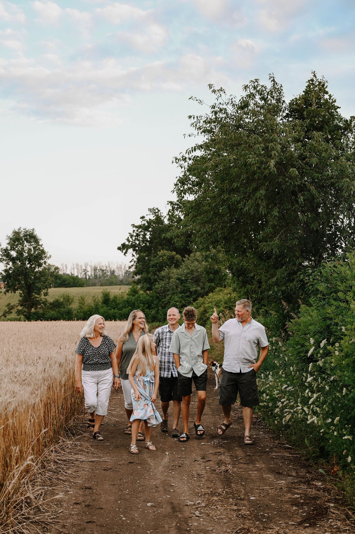 A group walking together on a dirt path through golden wheat fields at sunset.