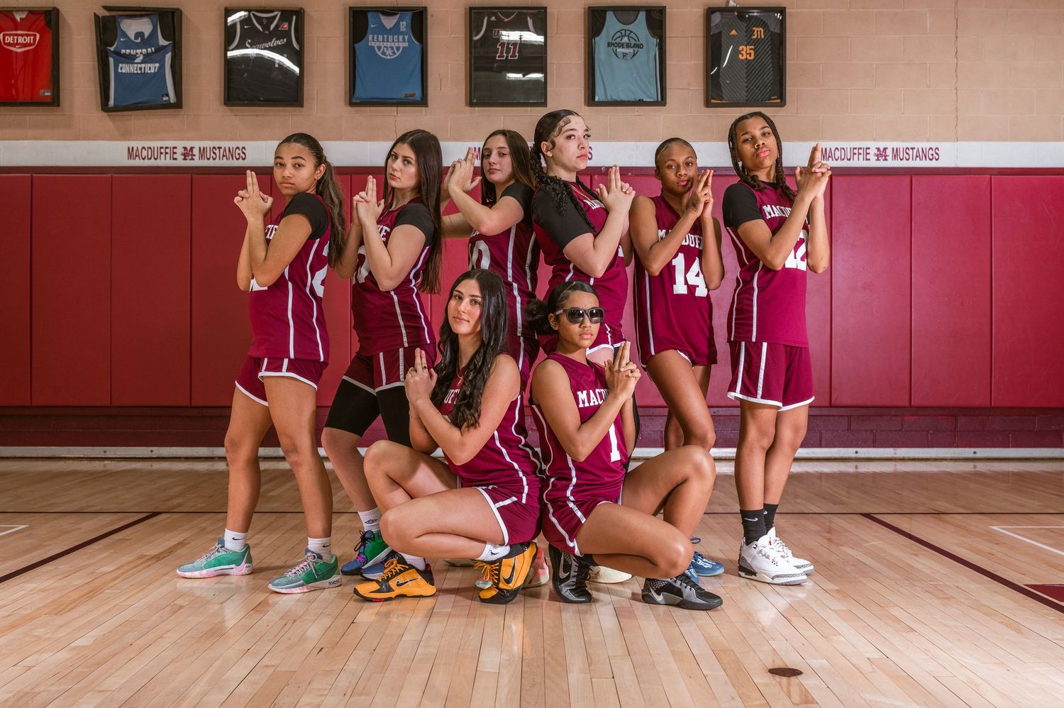 Basketball team in maroon uniforms poses together on gymnasium court with playful expressions.