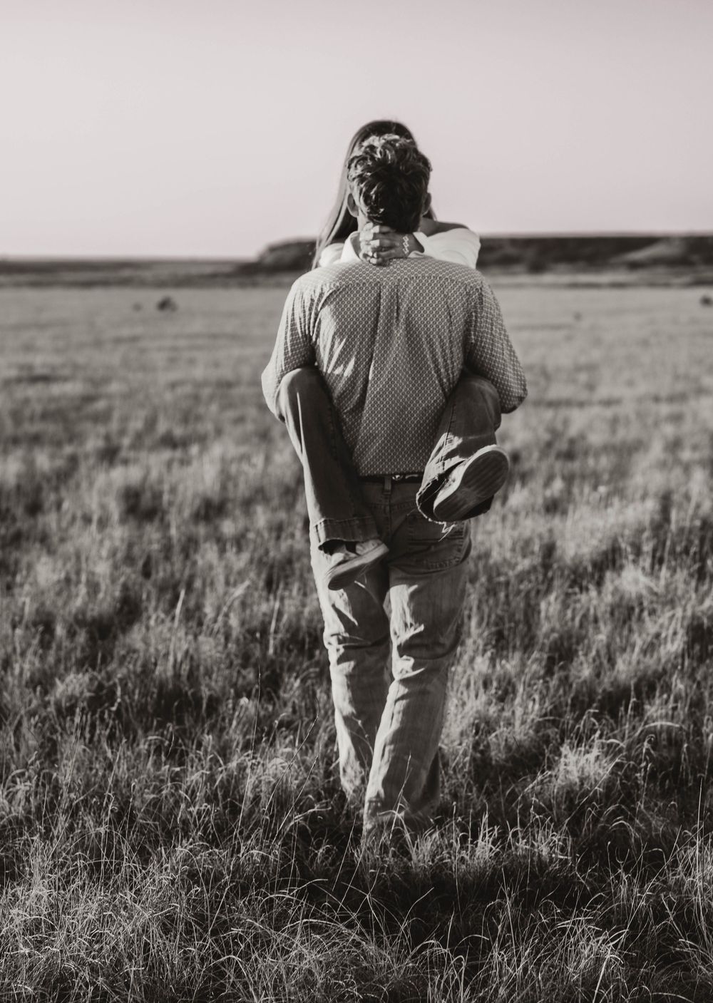 Black and white image sequence shows someone walking through tall grass in an open field or prairie landscape.
