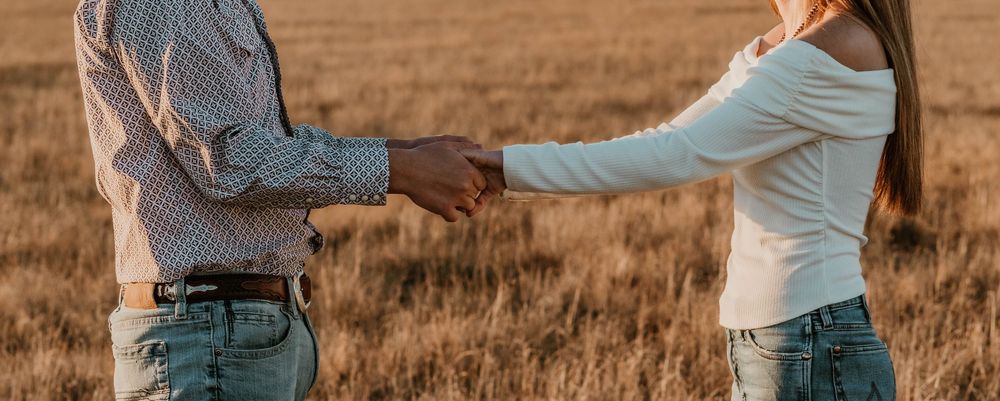 Romantic couple photoshoot in rustic western outfits at sunset in a desert field.