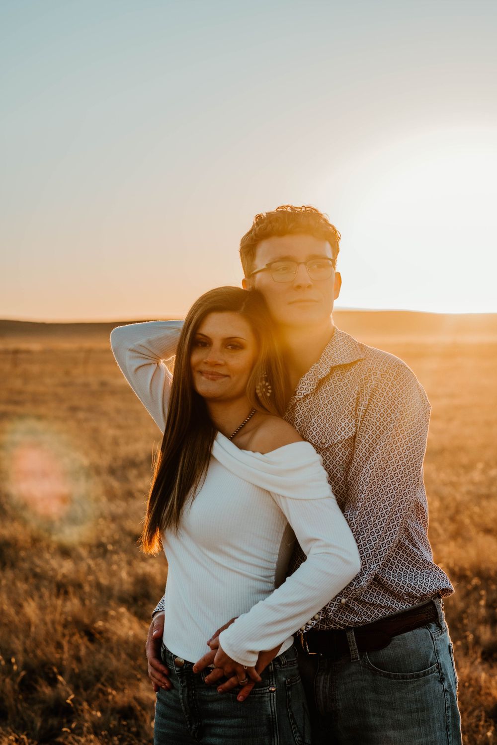 Two people share an intimate moment against a desert landscape backdrop during golden hour.