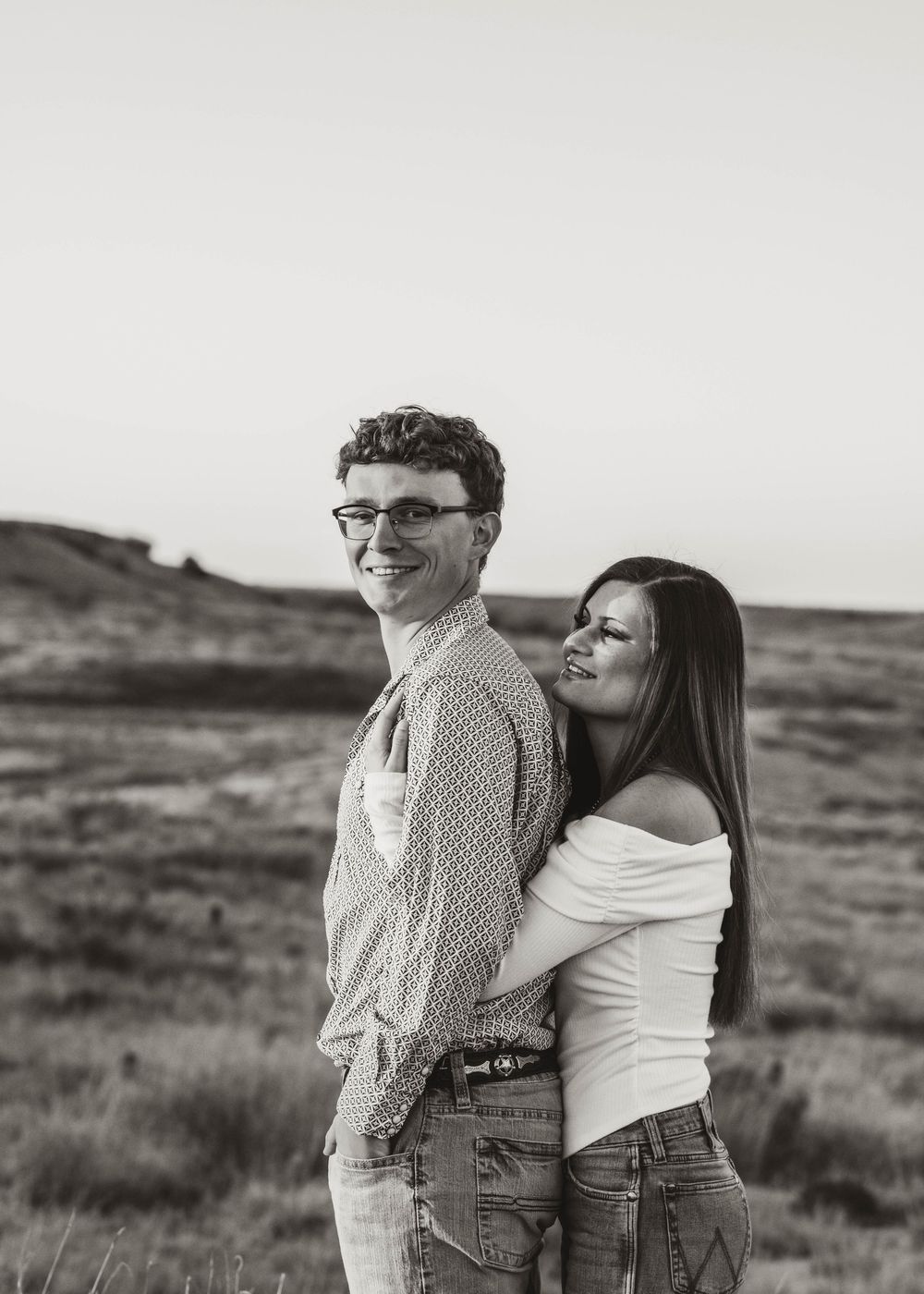 A romantic black and white portrait of a couple embracing in a desert landscape.