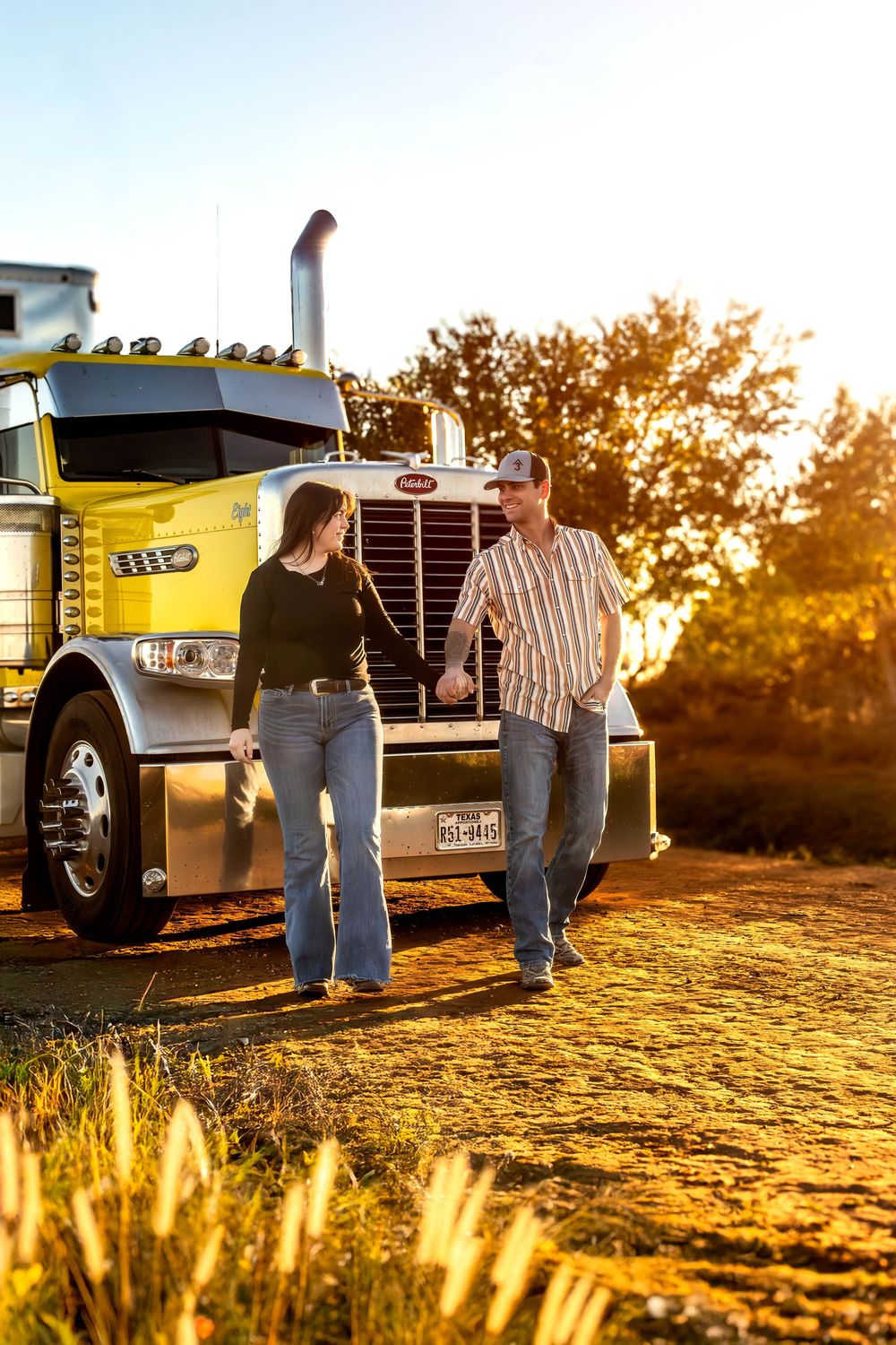 Couple shares tender moments near parked semi trucks at sunset.