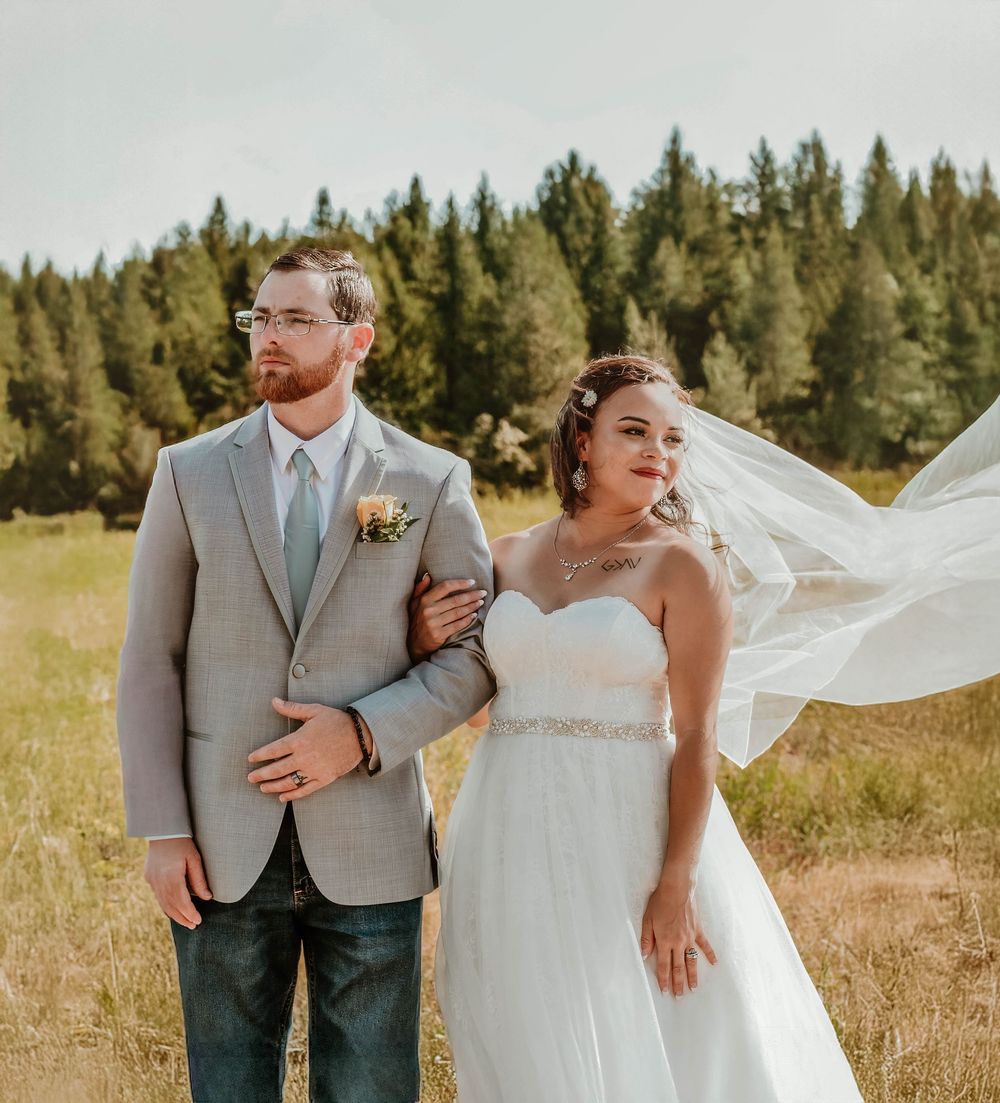 Wedding portraits captured in a rustic mountain meadow with flowing white veil and grey suit details.