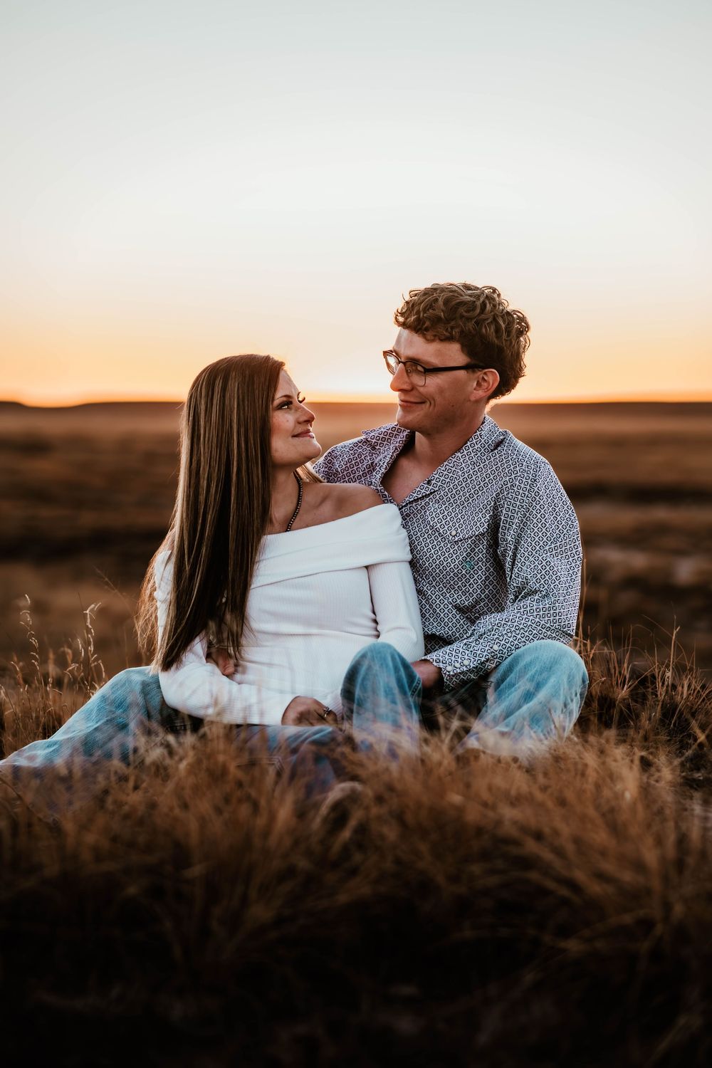 A couple sharing a tender moment while sitting in tall grass during golden hour.