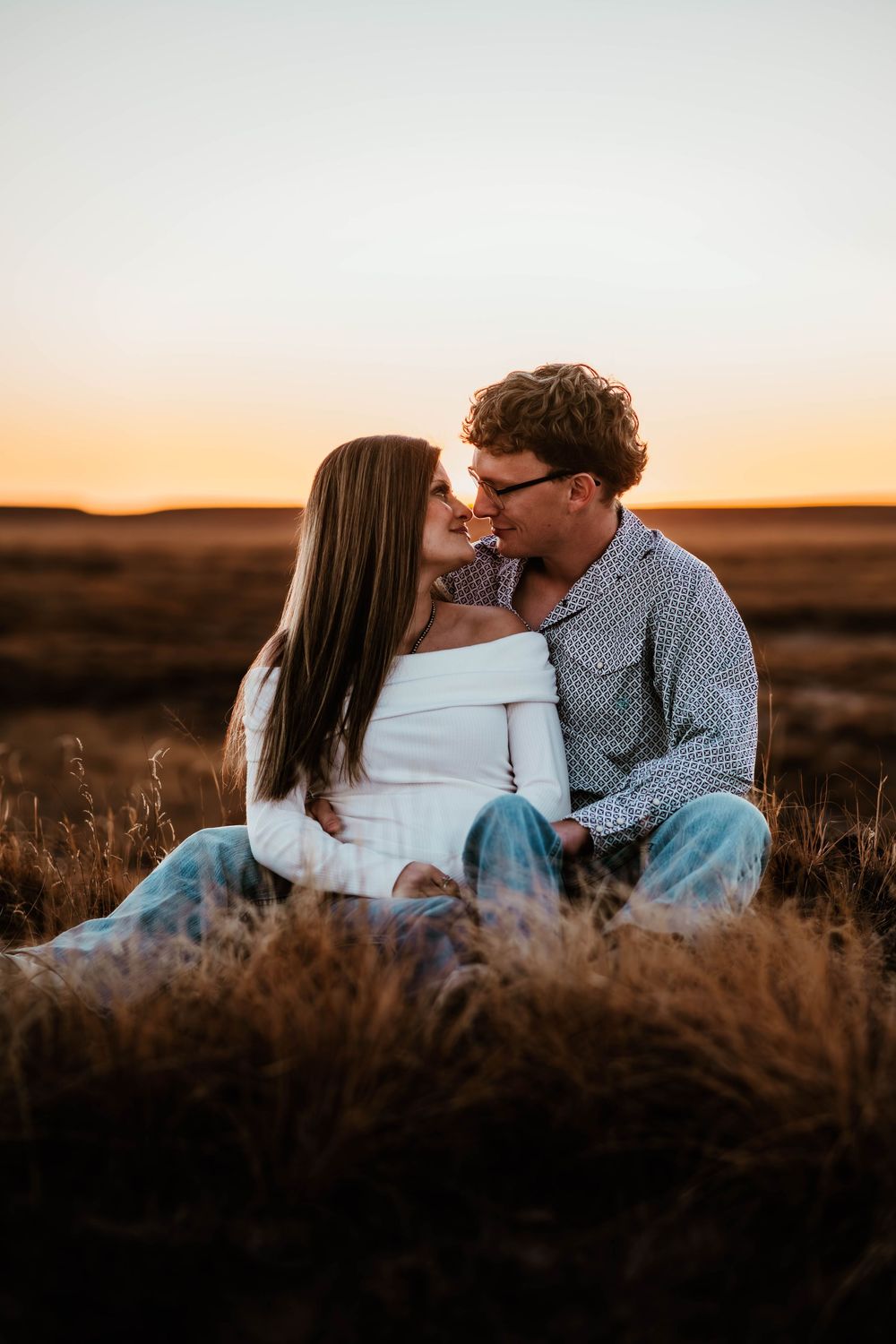 An intimate couple embraces in a wheat field against a warm sunset sky.