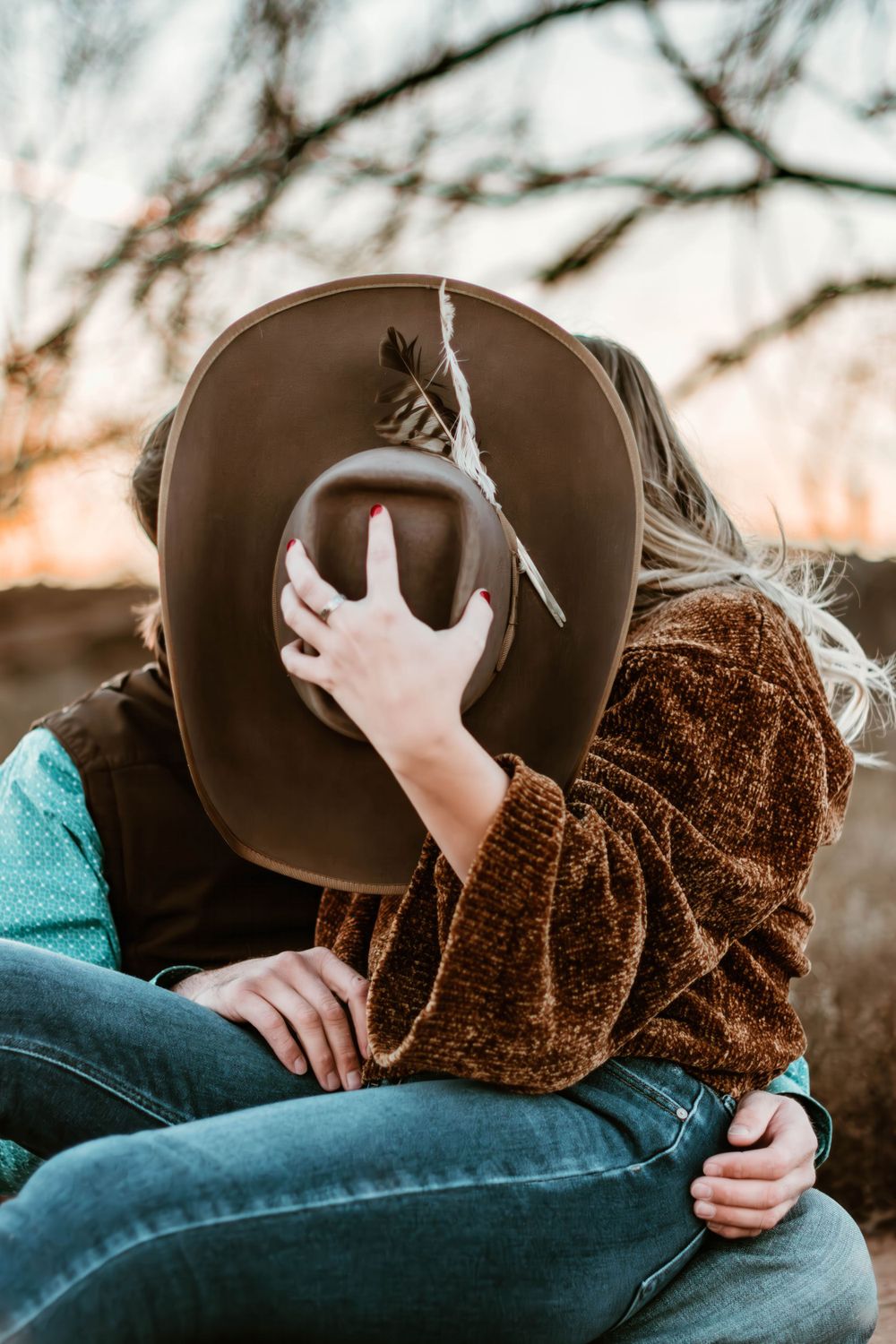 Two people share an intimate moment behind a brown cowboy hat at sunset.
