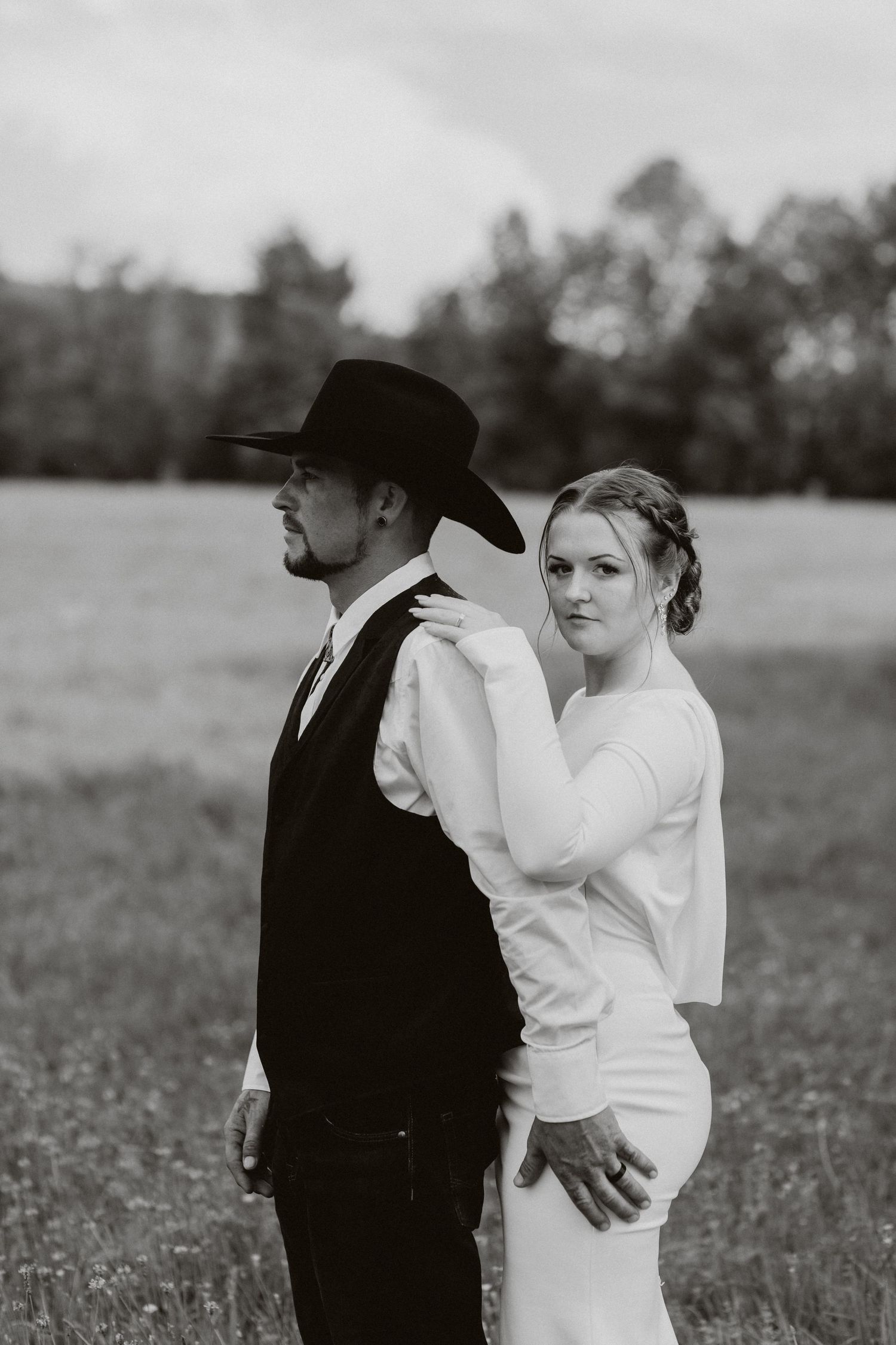 A romantic black and white portrait of a bride and groom in western attire standing back-to-back.